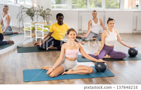 Multinational athletes sitting on floor in asana pigeon do body tilts to side, use fitball Multinational athletes sitting on floor in asana pigeon do body tilts to side, use fitball 137648218