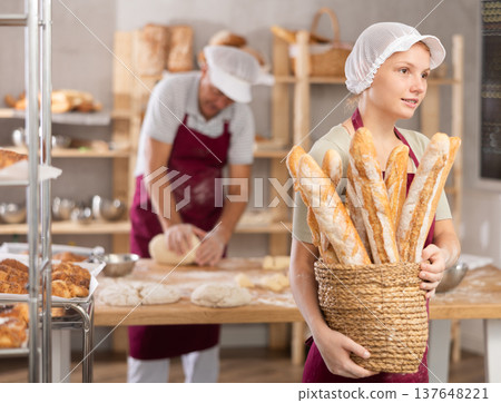 Young woman baker with basket of baguettes Young woman baker with basket of baguettes 137648221