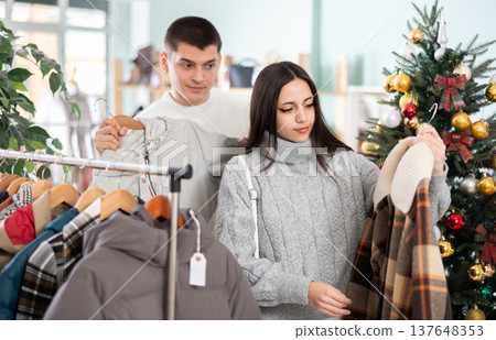 Young couple choosing coat or jacket for girl in clothing store Young couple choosing coat or jacket for girl in clothing store 137648353