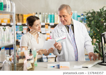 Senior man pharmacist use computer, girl intern with prescription Senior man pharmacist use computer, girl intern with prescription 137648357