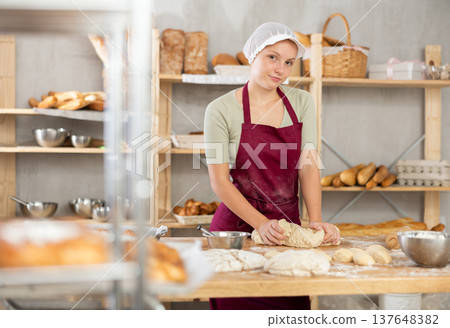 Young female baker kneading dough on table Young female baker kneading dough on table 137648382