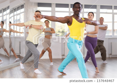 Positive African american man dancing and training movements Latin dance bachata during group class in choreography studio 137648467