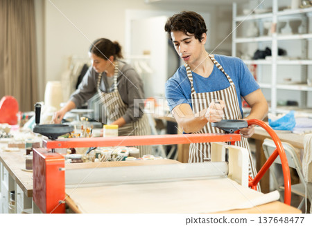 Young man rolling raw clay with mechanical slab roller 137648477