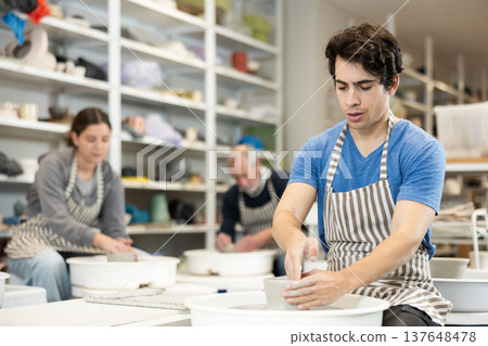 Young man shaping pottery on wheel in ceramics studio Young man shaping pottery on wheel in ceramics studio 137648478