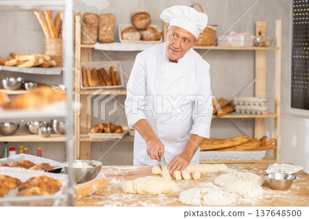 Baker in uniform cutting raw dough with knife to make croissants or buns Baker in uniform cutting raw dough with knife to make croissants or buns 137648500