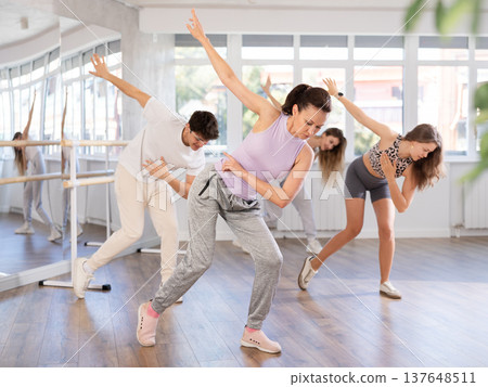 Cheerful young girl and multinational people training synchronous group choreography in dance studio 137648511