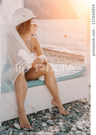 Woman hard hat beach sitting on a white cabana overlooking the sea during a golden sunset 137648854