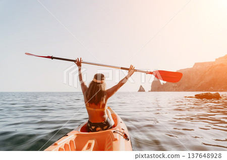 Kayaking Woman Ocean Paddle - Woman kayaking in the ocean raising her paddle in the air. Kayaking Woman Ocean Paddle - Woman kayaking in the ocean raising her paddle in the air. 137648928