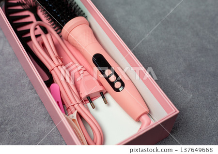 Box containing pink electric multi styler brush for hair styling. Everything in pink for pink lovers. Rich pink electric brush for girls and hair care. Complete set for creating perfect hairstyle 137649668