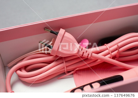 Pink power cord with a two-prong plug and various accessories placed inside a light pink box, emphasizing a clean and organized appearance suitable for modern home or office use Pink power cord with a two-prong plug and various accessories placed inside a light pink box, emphasizing a clean and organized appearance suitable for modern home or office use 137649676