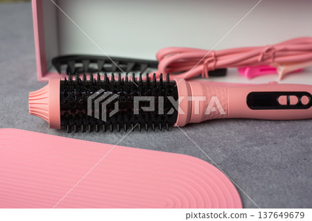 Multifunctional hair styling tool that combines the functions of several devices. Round, heated brush in pink case for women. Cute color for hairstyling device. Beauty concept Multifunctional hair styling tool that combines the functions of several devices. Round, heated brush in pink case for women. Cute color for hairstyling device. Beauty concept 137649679