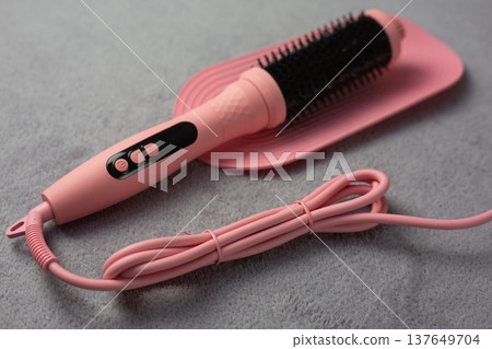 Pink electric hair styler with visible pink cord lies on protective mat. Powerful device ready for use, connected to electricity. Modern technology for effortless home hairstyling 137649704