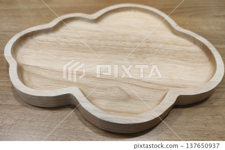 A carved wooden serving plate with decorative shape placed on a table, representing rustic restaurant tableware and antique-style food presentation 137650937