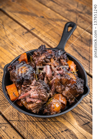 Braised beef oxtail stew with carrots and rosemary in cast iron skillet on rustic wooden table, rich dark sauce Braised beef oxtail stew with carrots and rosemary in cast iron skillet on rustic wooden table, rich dark sauce 137651240