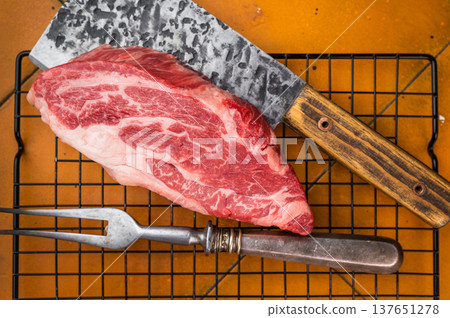 Raw beef chuck eye roll steak with marble structure and butcher cleaver. Uncooked beef cut prepared for grilling and frying. 137651278