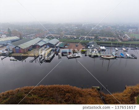 Aerial view of a misty marina in a Dutch town with boats, yachts, and warehouses. Foggy morning landscape in Muiden, Netherlands, featuring calm water reflections and traditional architecture. Aerial view of a misty marina in a Dutch town with boats, yachts, and warehouses. Foggy morning landscape in Muiden, Netherlands, featuring calm water reflections and traditional architecture. 137651657