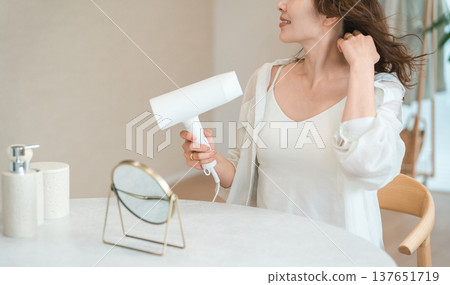 A woman blow-drying her hair with a hair dryer (hair care) A woman blow-drying her hair with a hair dryer (hair care) 137651719