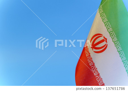 Iran flag against a blue sky background symbolizing political tension and crisis. Close-up view of the Iranian flag representing current geopolitical conflicts, social unrest, and international Iran flag against a blue sky background symbolizing political tension and crisis. Close-up view of the Iranian flag representing current geopolitical conflicts, social unrest, and international 137651786