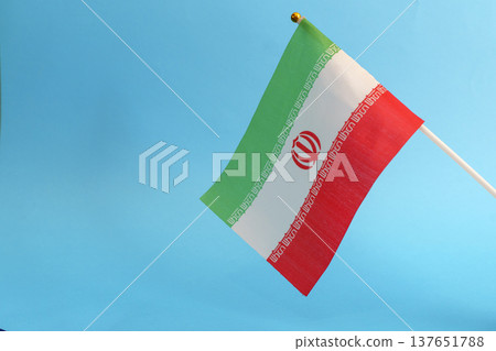 Iran flag against a blue sky background symbolizing political tension and crisis. Close-up view of the Iranian flag representing current geopolitical conflicts, social unrest, and international Iran flag against a blue sky background symbolizing political tension and crisis. Close-up view of the Iranian flag representing current geopolitical conflicts, social unrest, and international 137651788