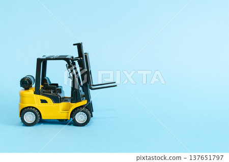 Forklift truck isolated on a blue background as a logic concept of warehouse storage. Conceptual photography showing a miniature toy loader symbolizing supply chain and logistics management with Forklift truck isolated on a blue background as a logic concept of warehouse storage. Conceptual photography showing a miniature toy loader symbolizing supply chain and logistics management with 137651797