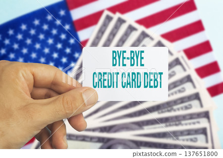 Human hand holding a plastic credit card with text bye bye credit card debt against a background of US dollar bills. Conceptual photography symbolizing financial freedom, paying off personal loans 137651800