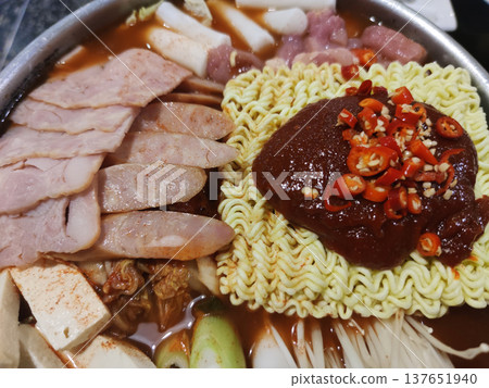A Korean-style spicy noodle hot pot topped with gochujang chili paste, sliced meat, tofu, and vegetables, representing homemade street food and restaurant-style Korean cuisine A Korean-style spicy noodle hot pot topped with gochujang chili paste, sliced meat, tofu, and vegetables, representing homemade street food and restaurant-style Korean cuisine 137651940