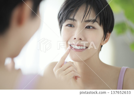 一位年輕女子在日常生活中對著鏡子檢查口腔衛生。 一位年輕女子在日常生活中對著鏡子檢查口腔衛生。 137652633
