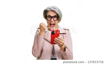 Senior woman cheering holding smartphone celebrating online win Senior woman cheering holding smartphone celebrating online win 137653738