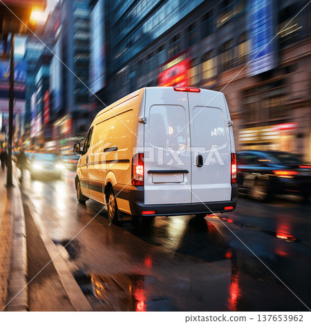 Delivery van drives through a busy street at dusk in a city with bright lights and reflections on wet pavement 137653962