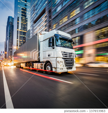Fast delivery truck driving through busy city streets at night with tall buildings and bright lights around it 137653963