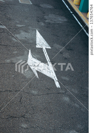 Road markings show direction on a cracked surface in urban area during daylight hours 137654764