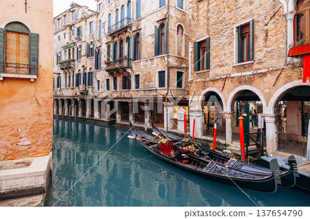 Gondola travels through narrow canals in Venice during a sunny day with clear water 137654790