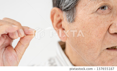 Senior man cleaning his ears with a cotton swab Senior man cleaning his ears with a cotton swab 137655187