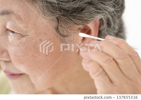 Senior woman cleaning her ears with a cotton swab Senior woman cleaning her ears with a cotton swab 137655316