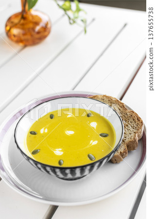 yellow organic pumpkin soup bowl with sourdough toast on restaurant white table outddor 137655738