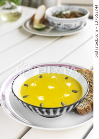 yellow organic pumpkin soup bowl with sourdough toast on restaurant white table outddor 137655744