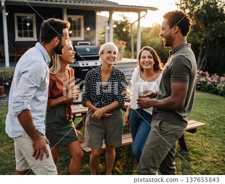 Friends gather in the backyard for drinks and laughter during an evening celebration while the sun sets behind them 137655843