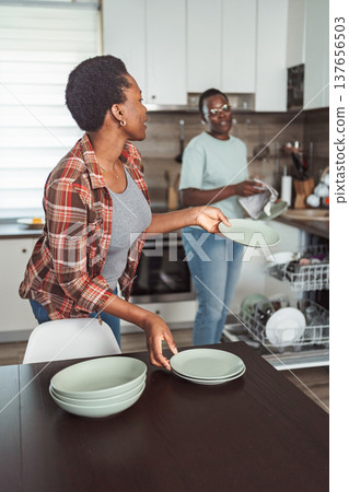 Two Young Women Arranging Dishes on the Table After Emptying the Dishwasher in a Modern Kitchen 137656503