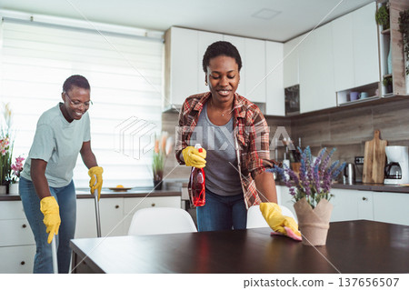 Two cheerful black women cleaning the kitchen table and floor Two cheerful black women cleaning the kitchen table and floor 137656507