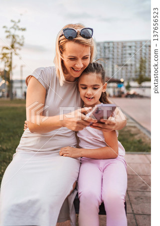 Mother and daughter using smartphone and smiling in a park 137656523