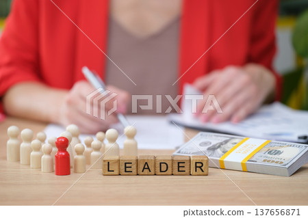 Conceptual illustration of leadership in business with wooden figures and money on a desk Conceptual illustration of leadership in business with wooden figures and money on a desk 137656871