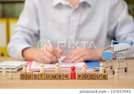 Business professional engaging in customer focus strategies with creative tools on a wooden desk Business professional engaging in customer focus strategies with creative tools on a wooden desk 137657043