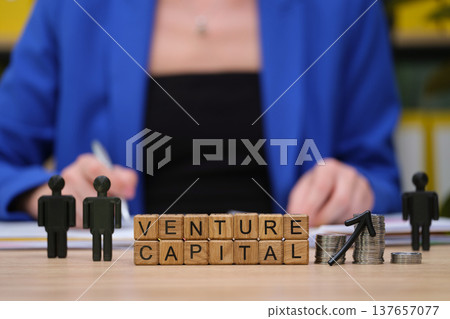 Venture capital discussion taking place with wooden blocks, miniature figures, and coins on a desk in a bright office setting Venture capital discussion taking place with wooden blocks, miniature figures, and coins on a desk in a bright office setting 137657077