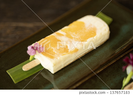 Plum marian flavored ice cream with cream cheese, white chocolate, and cracker base, with peanut butter, served on a stick. 137657183