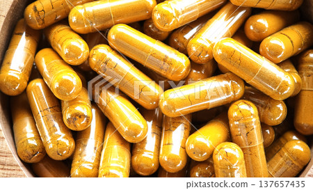 Herbal capsules containing turmeric powder in a wooden bowl. A natural anti-inflammatory dietary supplement. 137657435