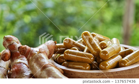 Herbal capsules containing turmeric powder in a wooden bowl. A natural anti-inflammatory dietary supplement. 137657436