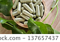 Herbal capsules containing Centella asiatica powder in a wooden bowl. A natural dietary supplement. 137657437