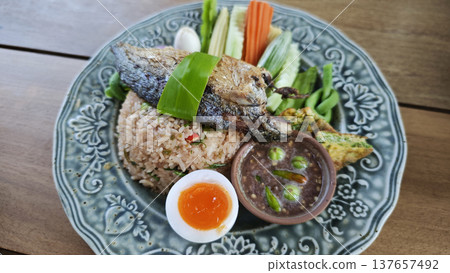 Thai fried rice with shrimp paste, topped with fried mackerel, vegetables, and egg. 137657492