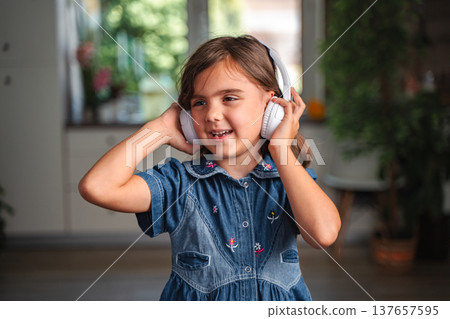 Little girl listening to music with headphones at home 137657595