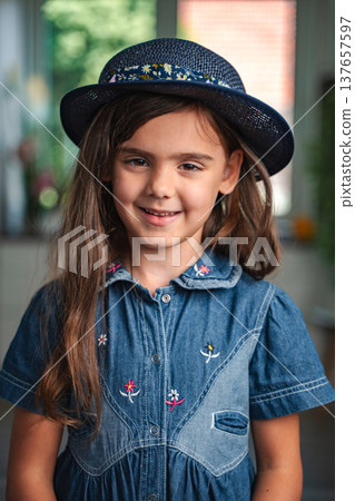 Portrait of smiling elementary age girl wearing blue hat and denim dress Portrait of smiling elementary age girl wearing blue hat and denim dress 137657597